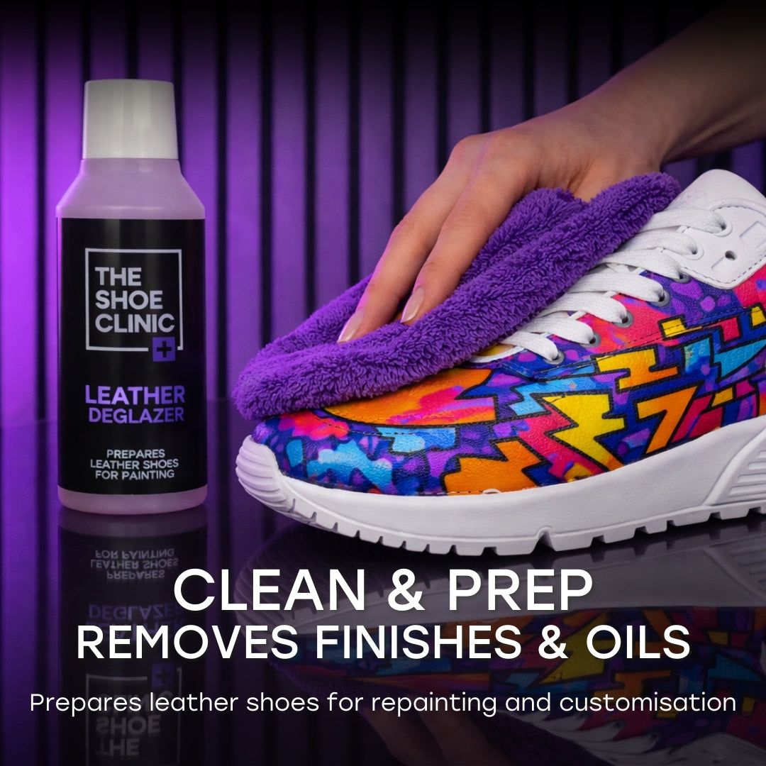 Colorful sneaker being cleaned with a cloth next to 'The Shoe Clinic' leather deglazer on a purple background.