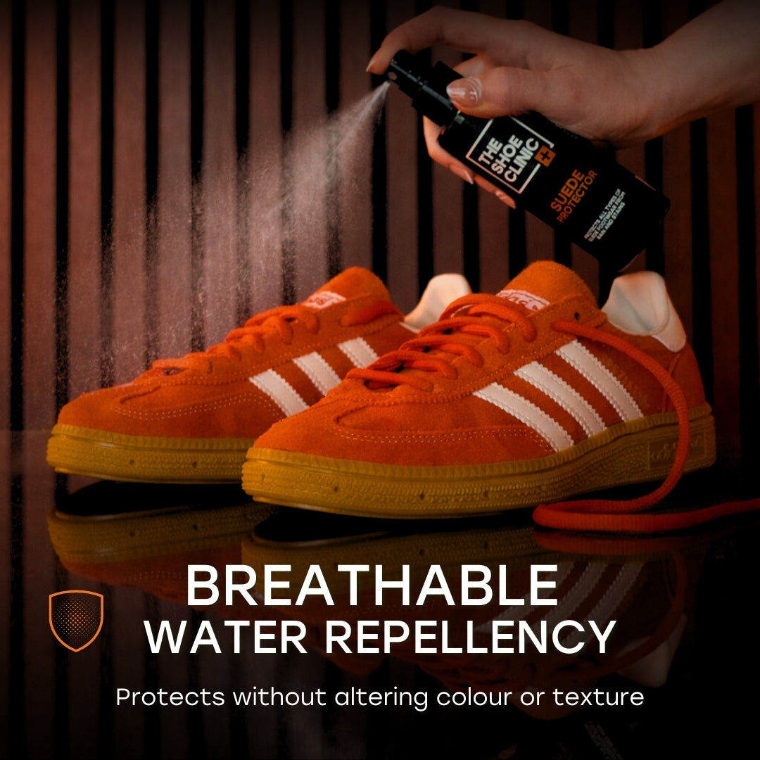 Orange shoes being sprayed with a product of 'Shoe Clinic, Suede Protector' on a dark background.